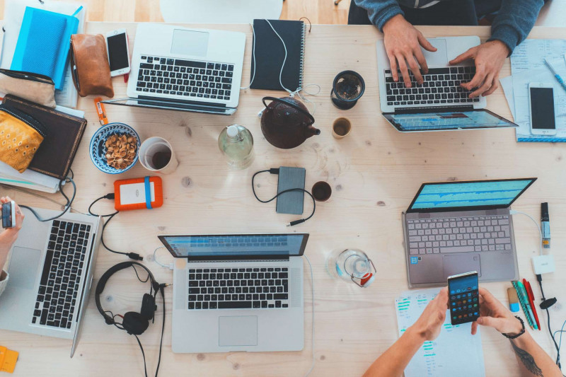 Decorative image: people working at a table surrounded by laptops, mobile phones and other technology